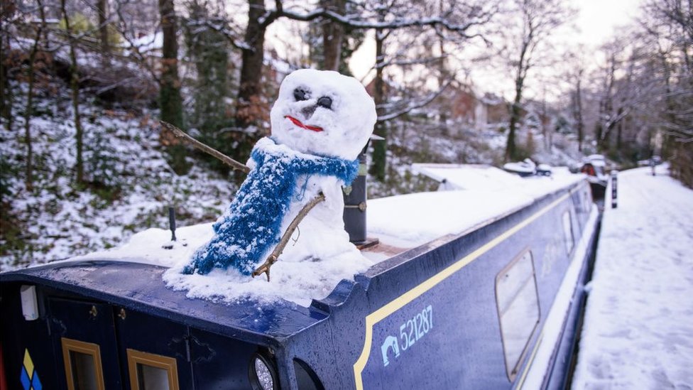 Снеговик сидит на лодке у канала в Лланголлене