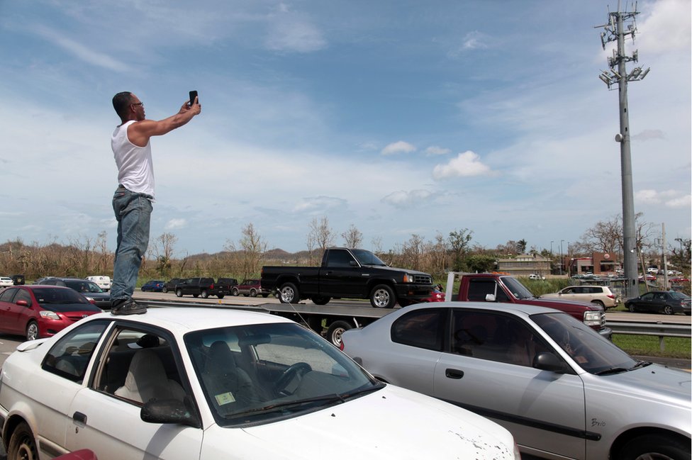 Hasta el 90% de las conexiones de celulares se perdieron tras el huracán María. Un hombre se sube en su coche buscando señal para el celular.