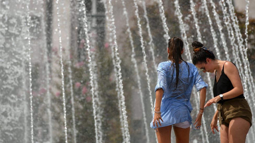 Dos mujeres refrescándose con chorros de agua de una fuente