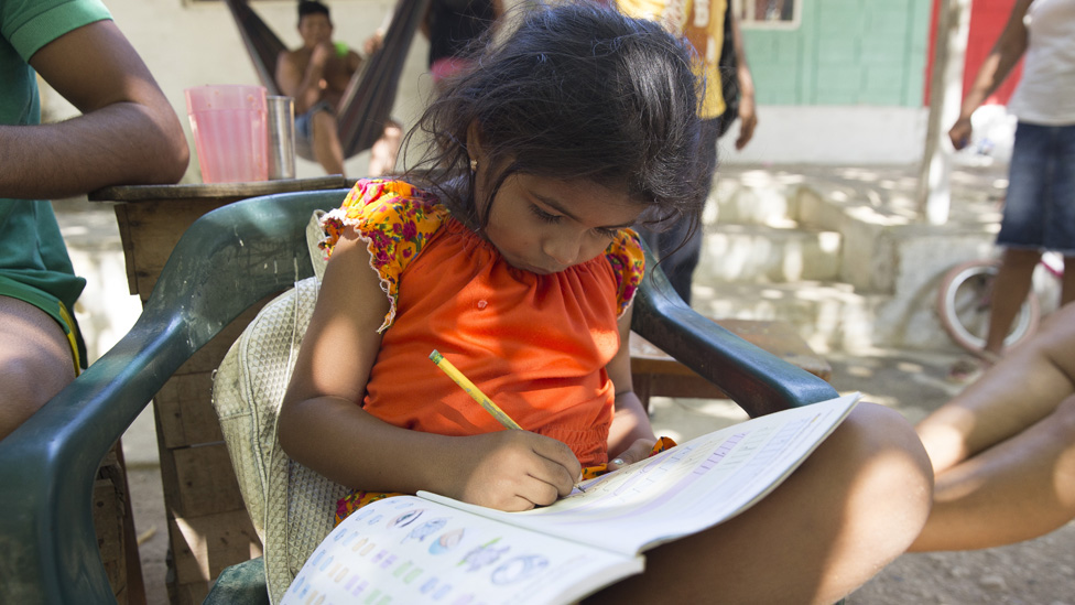 Семилетняя Шайла Монтерлаза, внучка перемещенной женщины, учится перед местной школой вместе со своей семьей