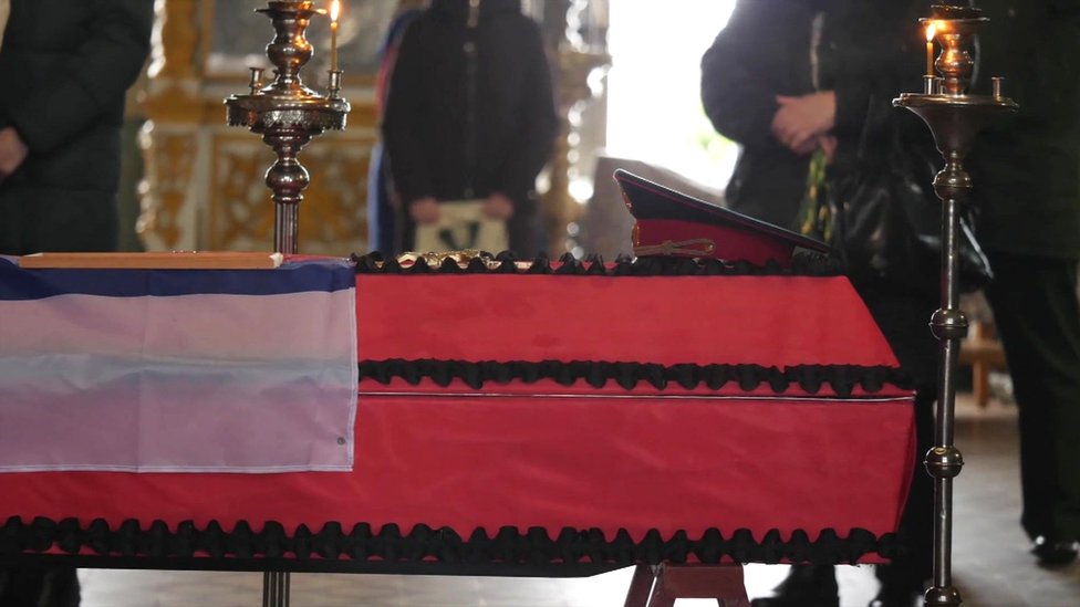 A coffin in red material covering with a serviceman's cap laid on top