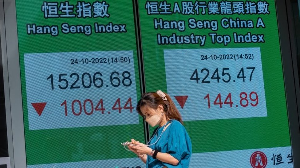 A woman walks past an electronic billboard displaying the Hang Seng Index figure in Hong Kong, China, 24 October 2022. The Hang Seng Index sank below 16,000 points for the first time in more than 13 years.