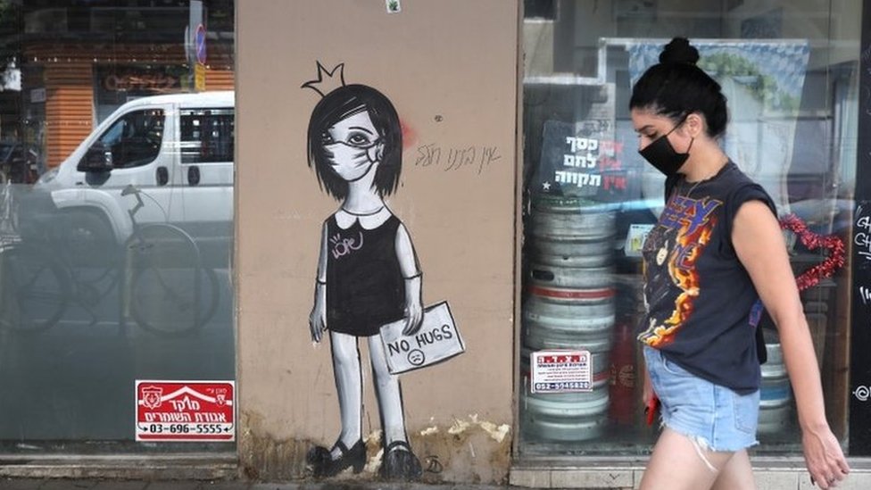 A woman walks by coronavirus graffiti in Tel Aviv (8 September 2020)