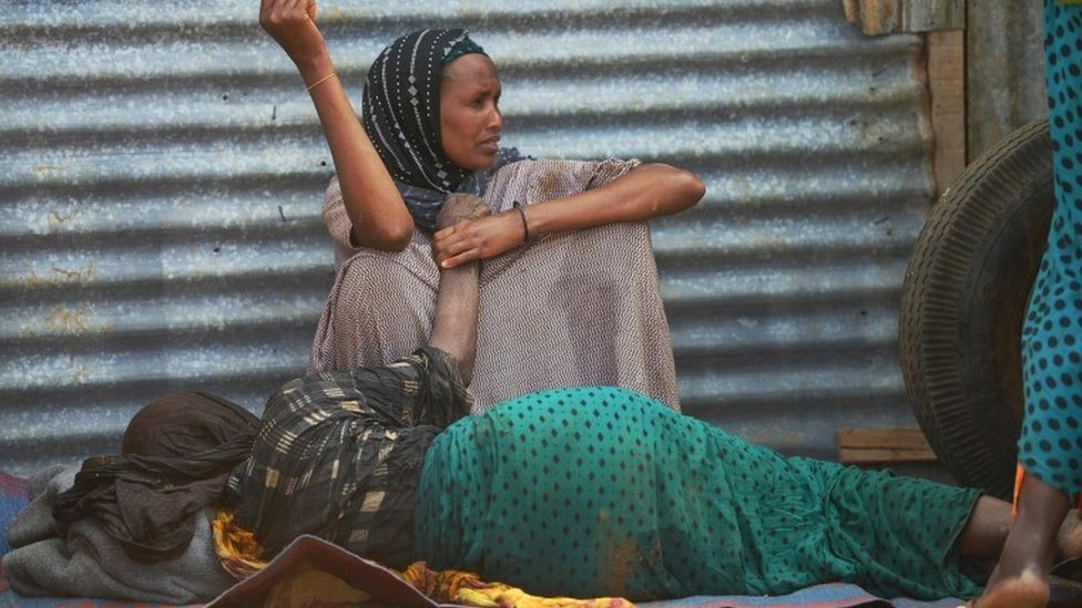Пожилая женщина, ослабленная голодом, лежит на земле, пока ее дочь наблюдает за ней в лагере для внутренне перемещенных лиц на окраине города Байдоа, столицы региона Бей на юго-западе Сомали