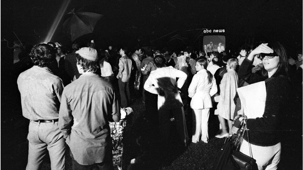 Зрители собираются в Центральном парке в Нью-Йорке, штат Нью-Йорк, чтобы посмотреть репортажи о высадке на Луну Аполлона-11 на одном из трех гигантских телевизионных экранов, установленных крупными сетями 20 июля 1969 года