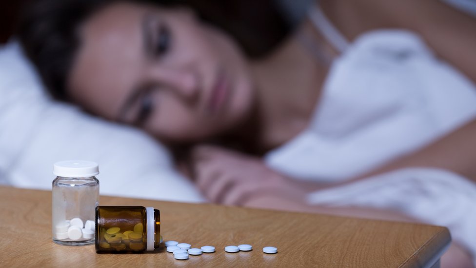 Mujer en la cama con unas píldoras para el sueño en la mesa de noche
