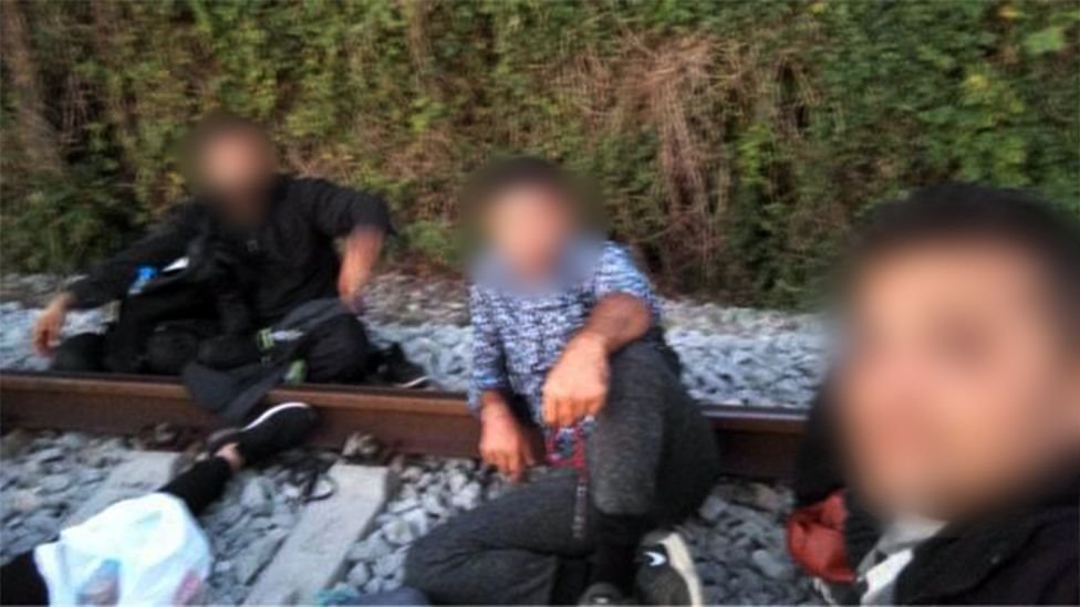 Three migrants pose in a selfie on some rail tracks (faces are obscured to prevent identification)