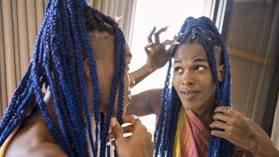 Mulher negra olhando suas tranças azuis no espelho