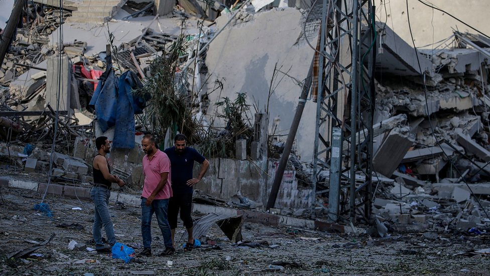 Palestinians next to a demolished building in Gaza City