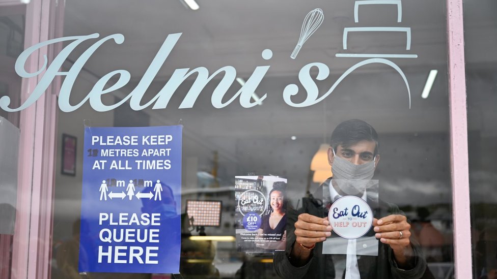 Канцлер казначейства Риши Сунак помещает наклейку «Поесть, чтобы помочь» в витрине своего предприятия во время визита в Ротсей на острове Бьют, Шотландия.