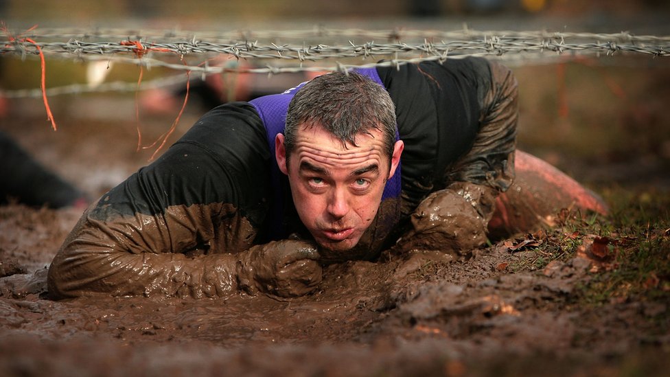 El primer desafío pasa por superar tus miedos según promovió Billy Wilson, el creador de Tough Guy. Persona pasando por debajo de alambres de púas.