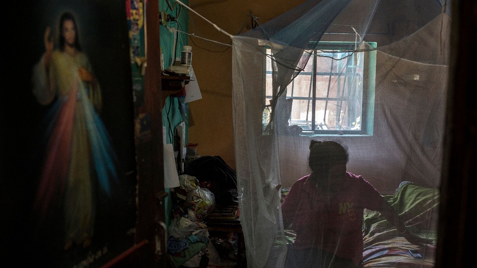 A woman sitting on her bed around which she placed a mosquito net