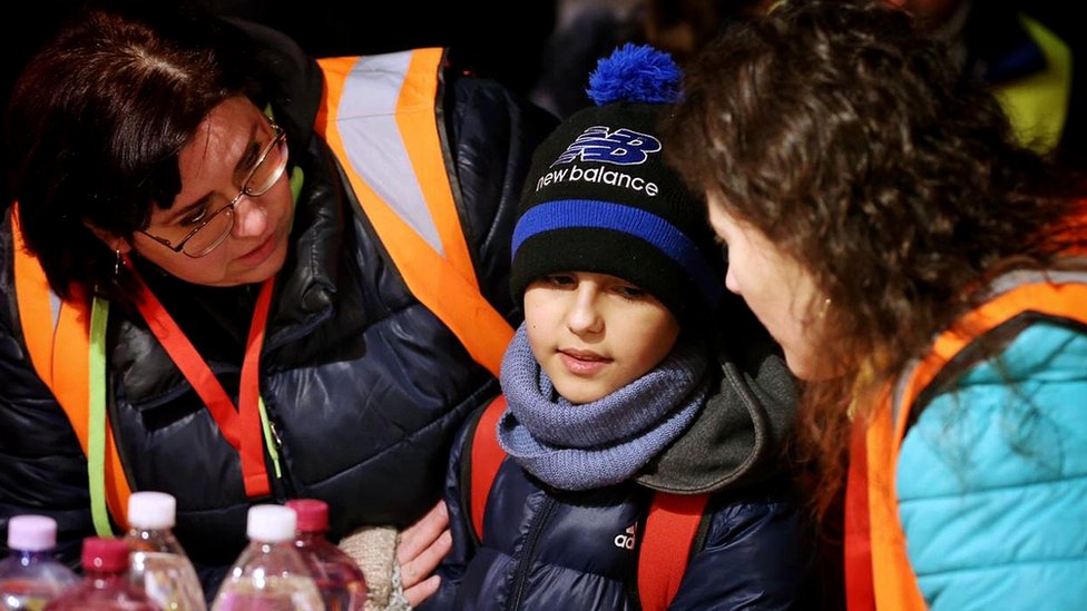 Dois voluntários ao redor de um garoto de 11 anos com roupas de frio