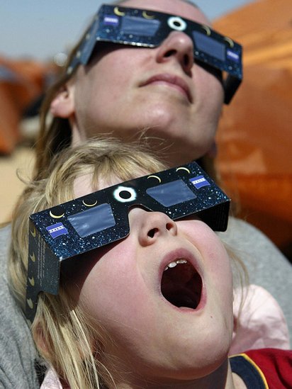 Niña y mujer viendo eclipse sorprendidas.