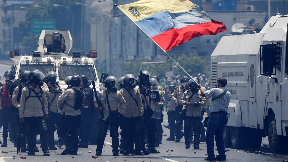 La oposición venezolana acusa al gobierno de recurrir de forma excesiva a la represión de las protestas. Un hombre ondea la bandera de Venezuela ante un grupo de guardias nacionales con equipos antimotines.