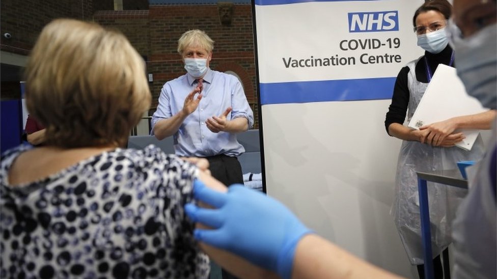 Prime Minister Boris Johnson applauds after nurse Rebecca Cathersides administers the vaccine to Lyn Wheeler