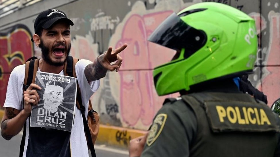 Демонстрант с плакатом с изображением покойного Дилана Круза кричит на полицию во время марша против правительства президента Колумбии Ивана Дуке во время национальной забастовки в Кали 27 ноября 2019 г.