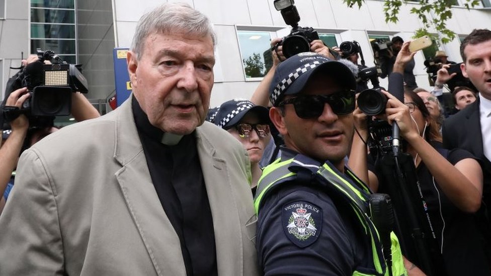 Джордж Пелл покидает судебное заседание в Мельбурне в феврале в сопровождении полиции и представителей СМИ