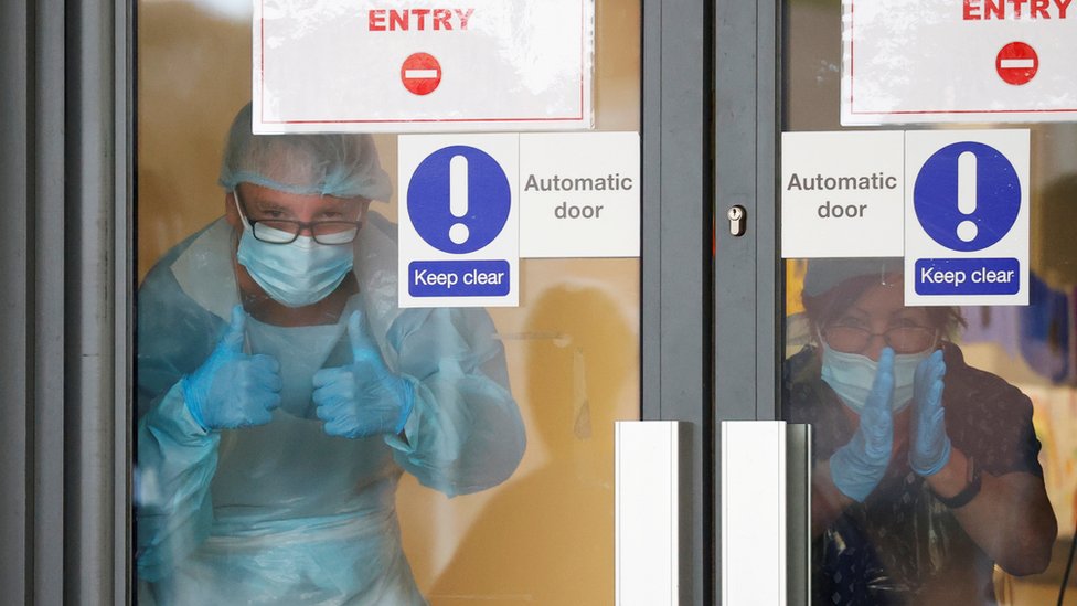 Медицинский персонал в СИЗ хлопает в ладоши через стеклянную дверь