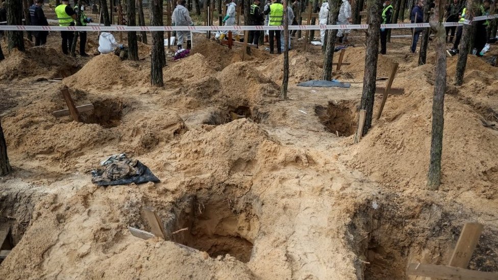Police and experts work at a place of mass burial during an exhumation in Izyum, 17 September 2022.