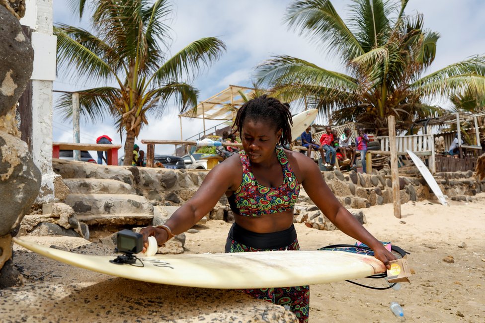 Khadjou Sambe waxes her surfboard on the beach