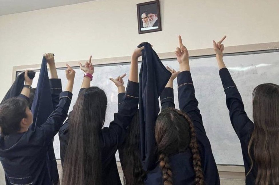 Estudiantes levantando el dedo medio, haciendo una seña que es considerada obscena, ante los retratos del ayatolá Jamenei y del fundador de la República Islámica, el ayatolá Ruholá Jomeini.