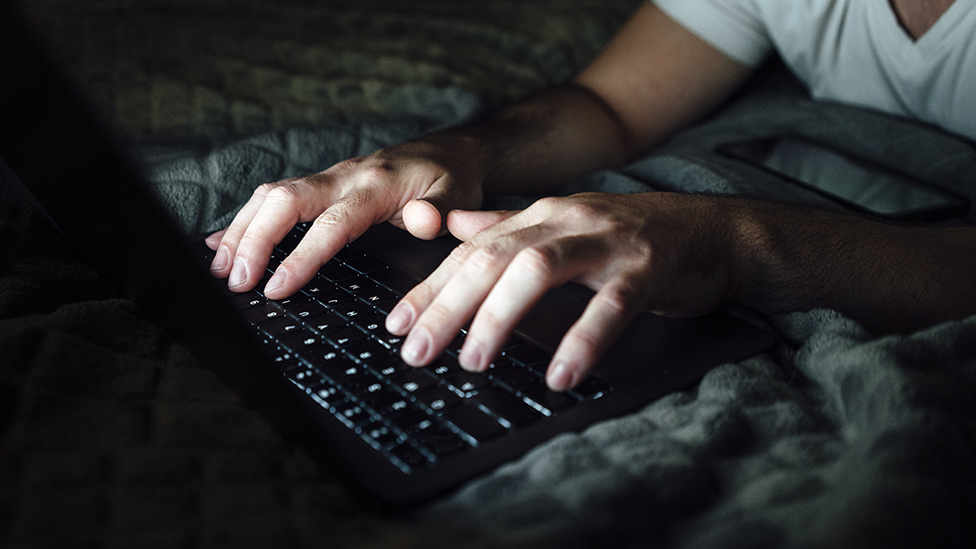 Un hombre tipeando en un teclado a oscuras.