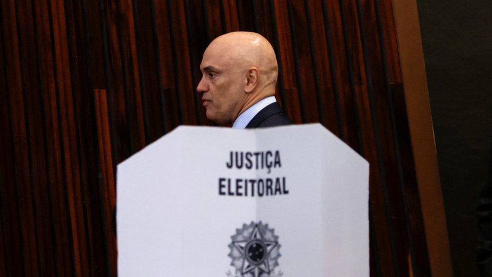 O presidente do TSE, ministro Alexandre de Moraes, em frente a painél com símbolo da Justiça Eleitoral