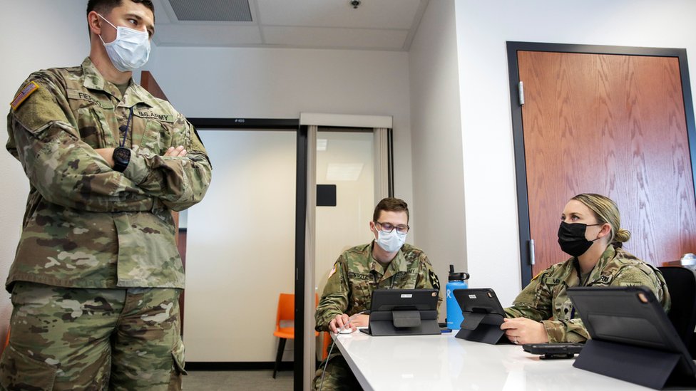 Члены национальной гвардии США проходят подготовку к выполнению задания в Тамвотере, штат Вашингтон - один человек стоит в комнате, а двое сидят, все в масках
