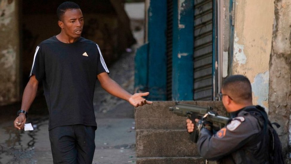 Полицейский направляет свое оружие в человека после беспорядков во время протеста в Рио-де-Жанейро 9 августа 2019 г.