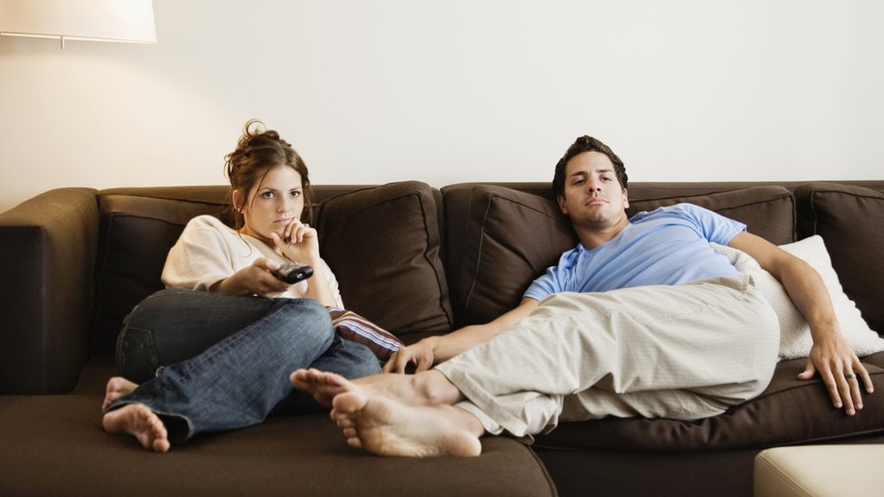 Una mujer y un hombre echados en un sofá mirando televisión