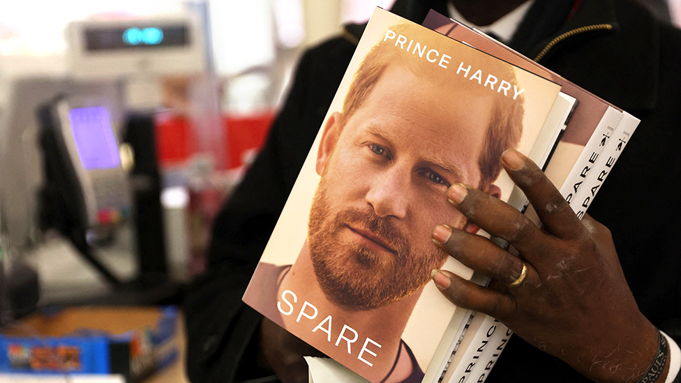 Prof Chris Imafidon holds three copies of the book Spare at the WHSmith bookstore, at Victoria Station in London, on 9 January, 2023