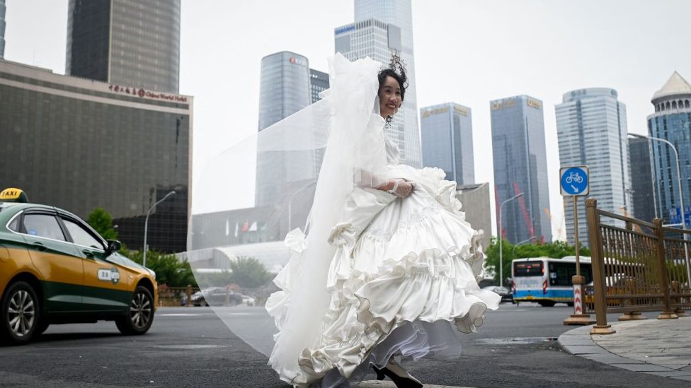 A woman crosses a road before posing for wedding photos in Beijing on May 5, 2023.