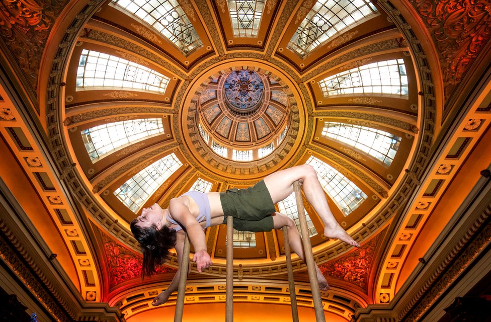 Acrobat Alyssa Moore is held up by poles with an ornate ceiling in the background