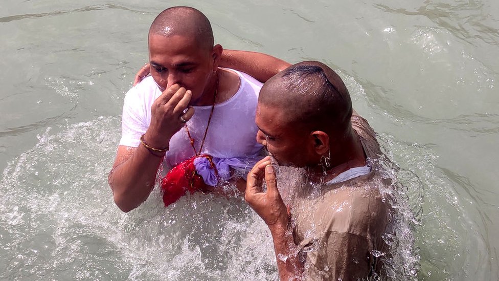 Devotos vestidos tomam banho no rio Ganges, na Índia