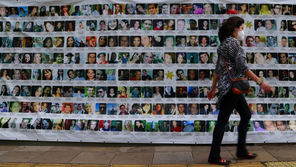 Una mujer pasa frente a un mural con fotos de las víctimas de la tragedia de la discoteca.