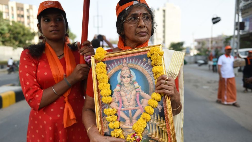 Женщина держит плакат с изображением индуистского бога в рамке, за ней следует другая женщина