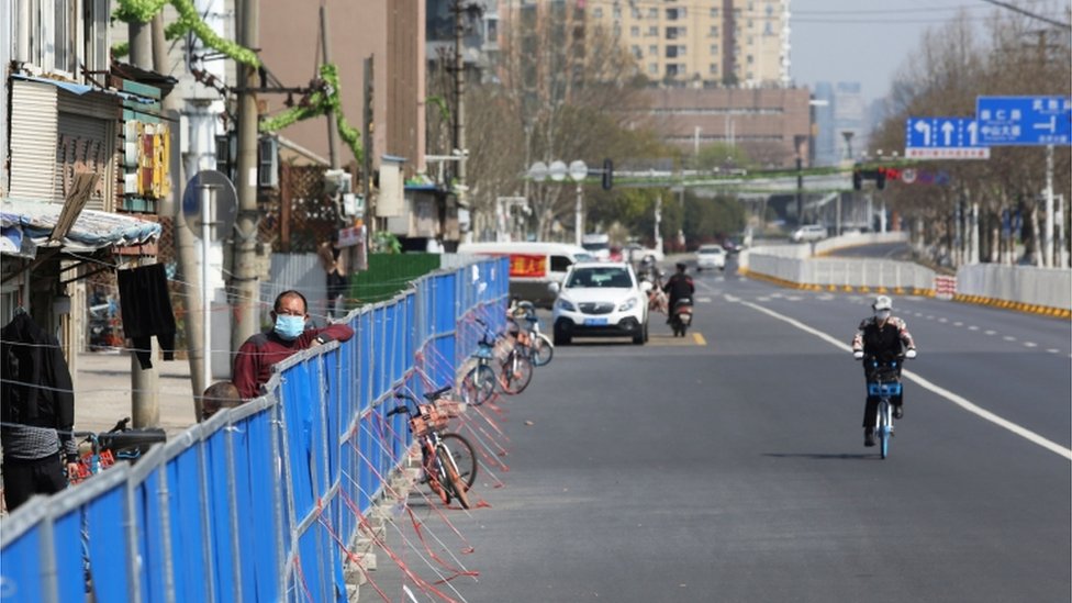 На этой фотографии, сделанной 17 марта 2020 года, изображен мужчина, просматривающий барьер, установленный для предотвращения входа или выхода людей из жилого комплекса в Ухане, в центральной провинции Китая Хубэй.