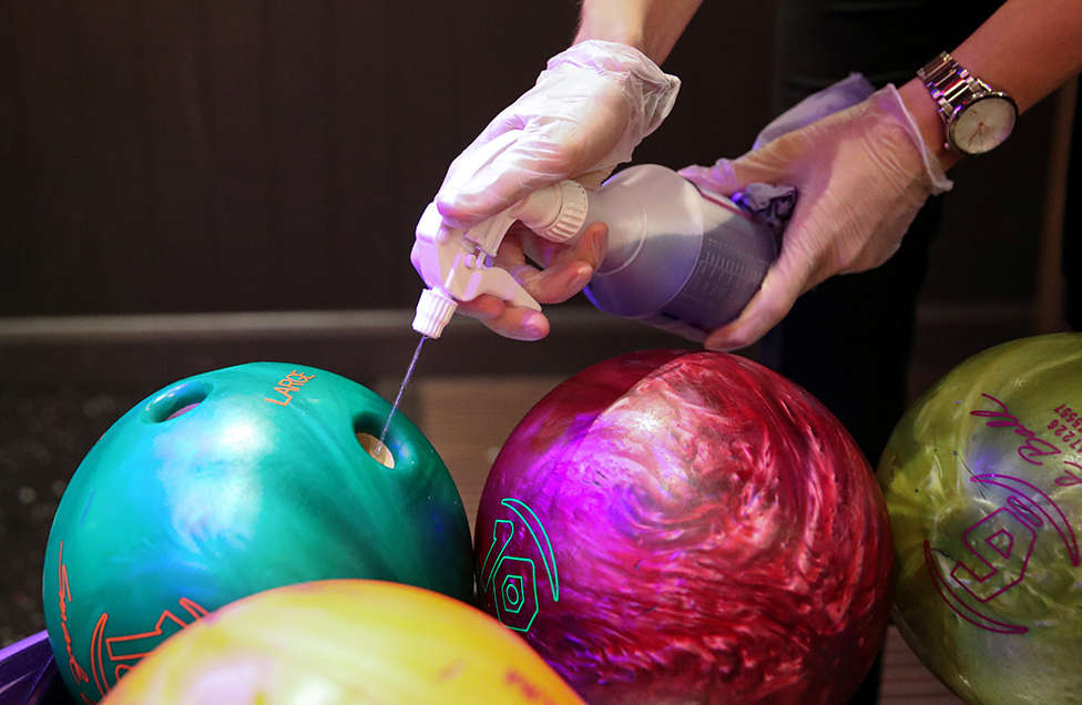 A person sprays disinfectant on to a bowling ball