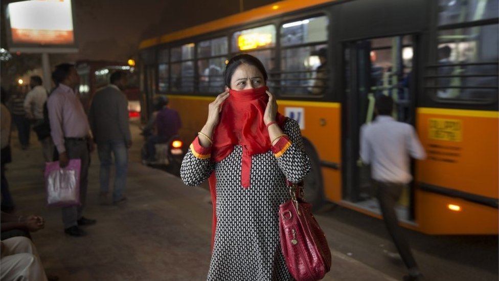Индийская женщина закрывает лицо от загрязнения, ожидая на автобусной станции в Нью-Дели, Индия.