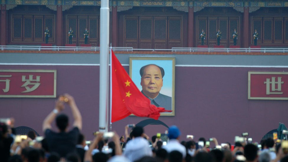Una fotografía de Mao Zedong a las puertas de la Ciudad Prohibida en Pekín, frente a una multitud de personas con celulares.