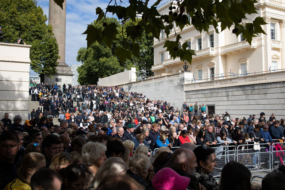 A crowd stands around the King George VI & Queen Elizabeth Memorial on The Mall.