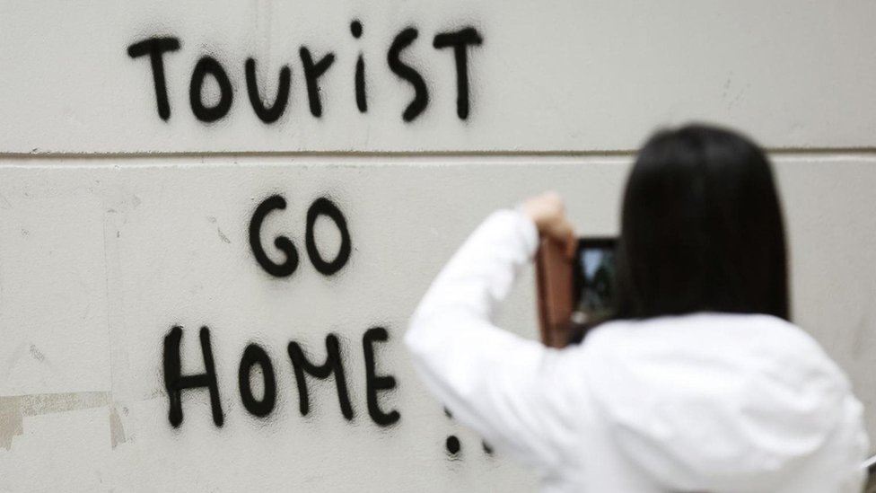 سائحة تلتقط صورة لكتابات جدارية تحض السياح على مغادرة برشلونة، في إسبانيا العام الماضي