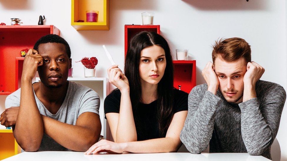 A woman sits between two men holding up a pregnancy test