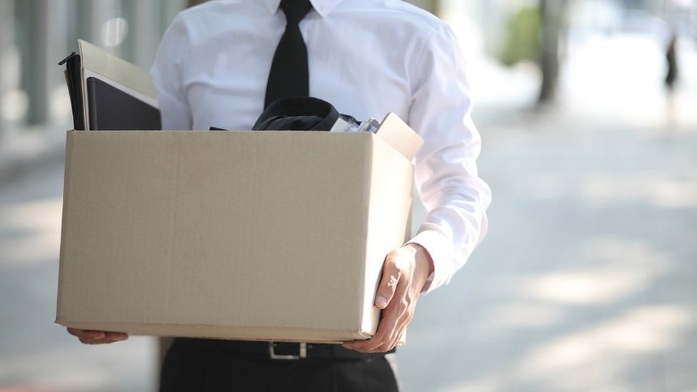 Homem engravatado segura uma caixa com seus materiais de escritório após ser demitido