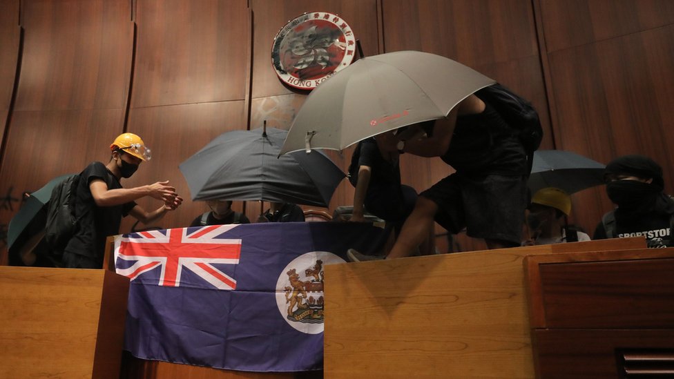 Протестующие прикрепляют британский колониальный флаг к трибуне парламента после того, как они ворвались в штаб-квартиру правительства в Гонконге 1 июля 2019 г.,