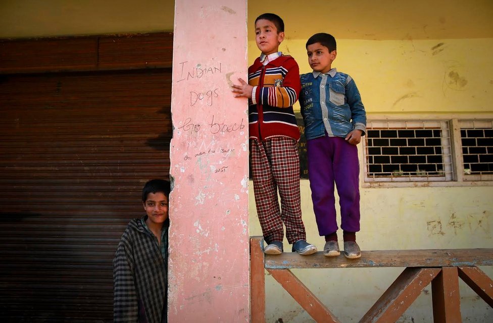 Дети стоят рядом с антииндийскими граффити на стене школы
