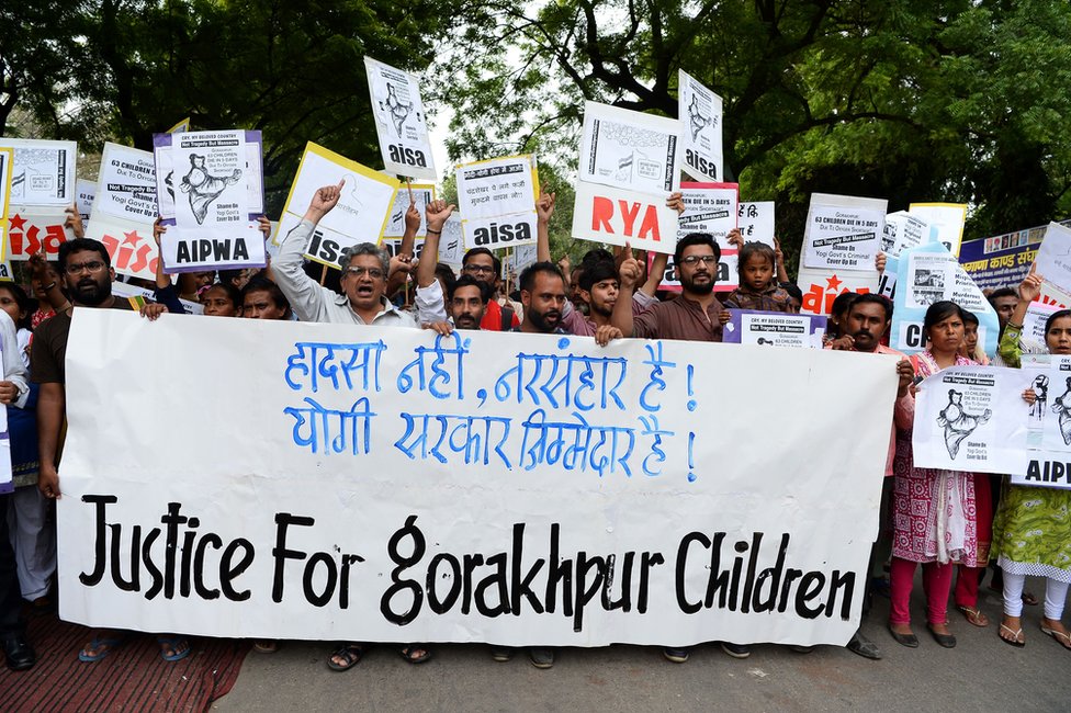 Протестующие держат плакаты и выкрикивают лозунги против гибели по меньшей мере 64 детей в больнице Баба Рагхав Дас в Горакхпуре.