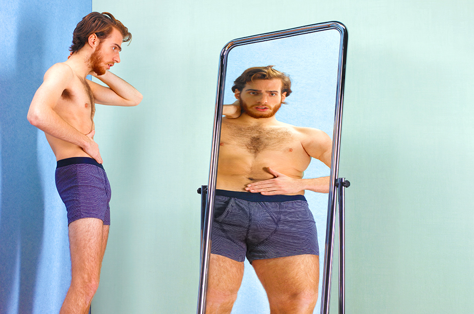 Un joven mirando una imagen más grande suya en un espejo