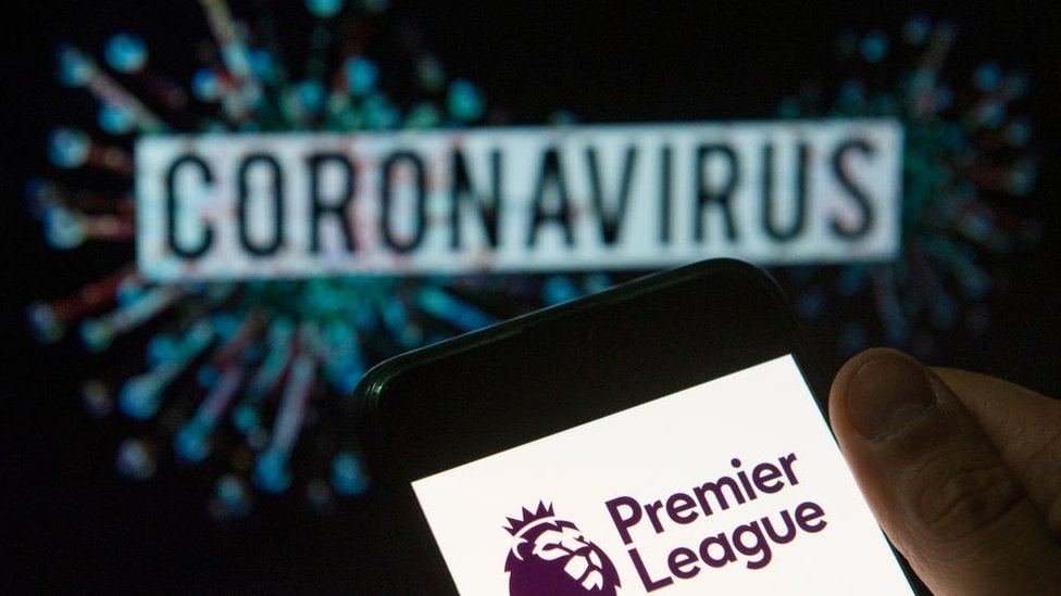 شعار الدوري الإنجليزي الممتاز يظهر في هاتف ذكي ويقابله عبارة "فيروس كورونا"